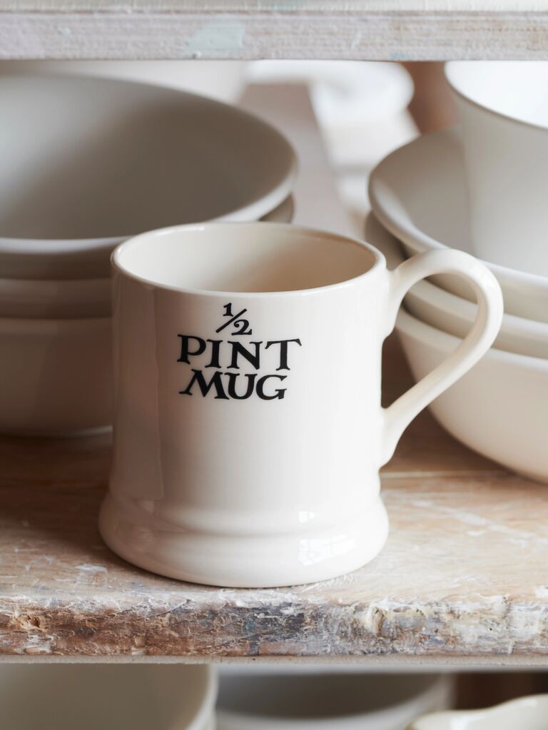 Half-pint white ceramic mug on rustic wooden shelf, surrounded by stack of elegant white bowls, showcasing minimalist design.