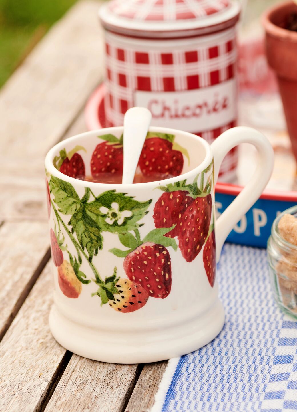 Ceramic mug with vibrant strawberry pattern, providing a charming and colourful touch to a rustic dining setting.