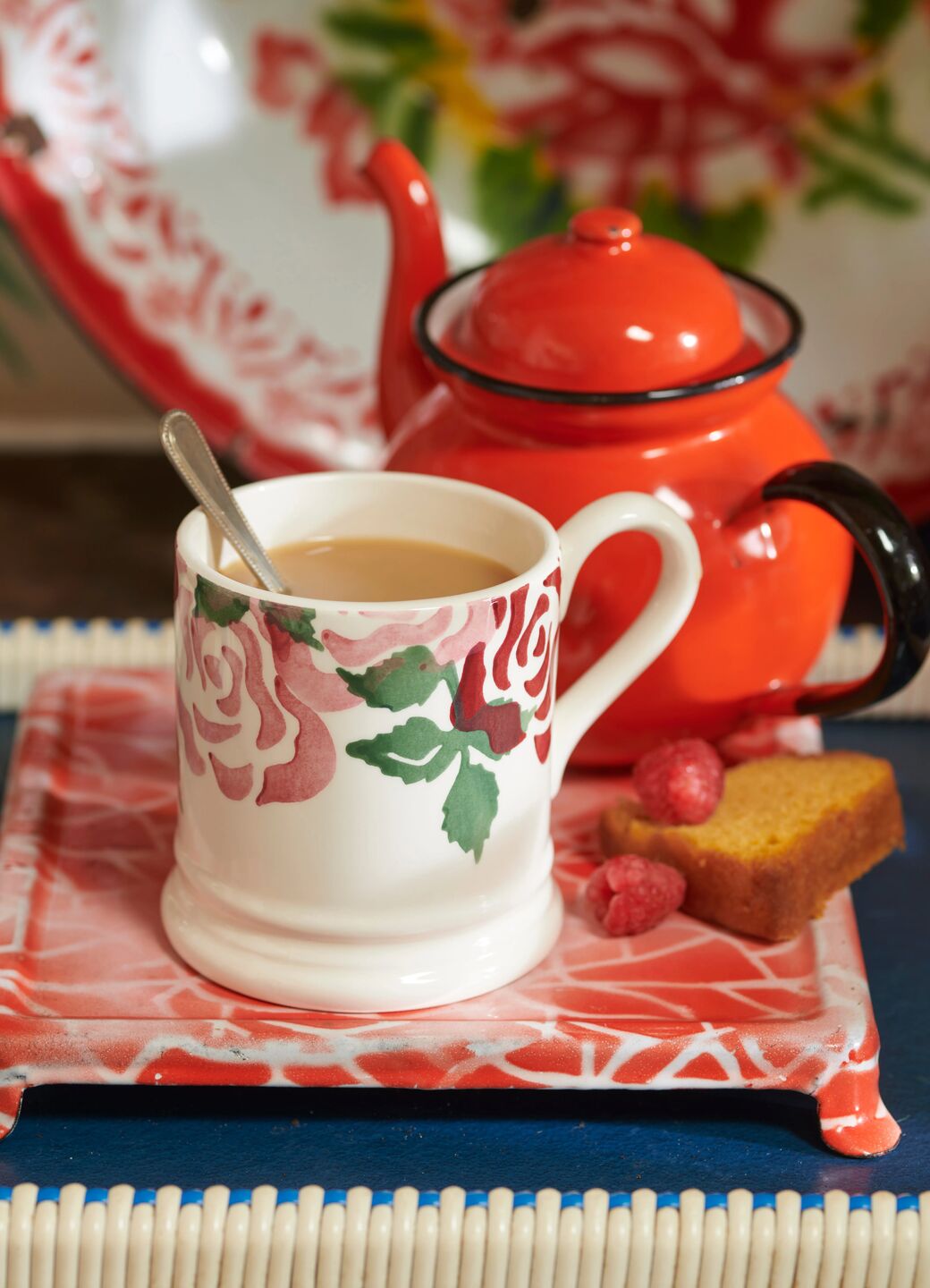 Floral-patterned ceramic mug with tea and a vintage red teapot on a decorative tray for a cosy tea setting.