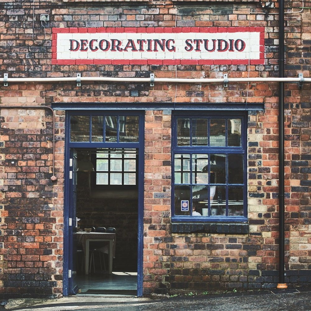 Vintage brick facade of a decorating studio with blue-painted windows and door, evoking an industrial charm.
