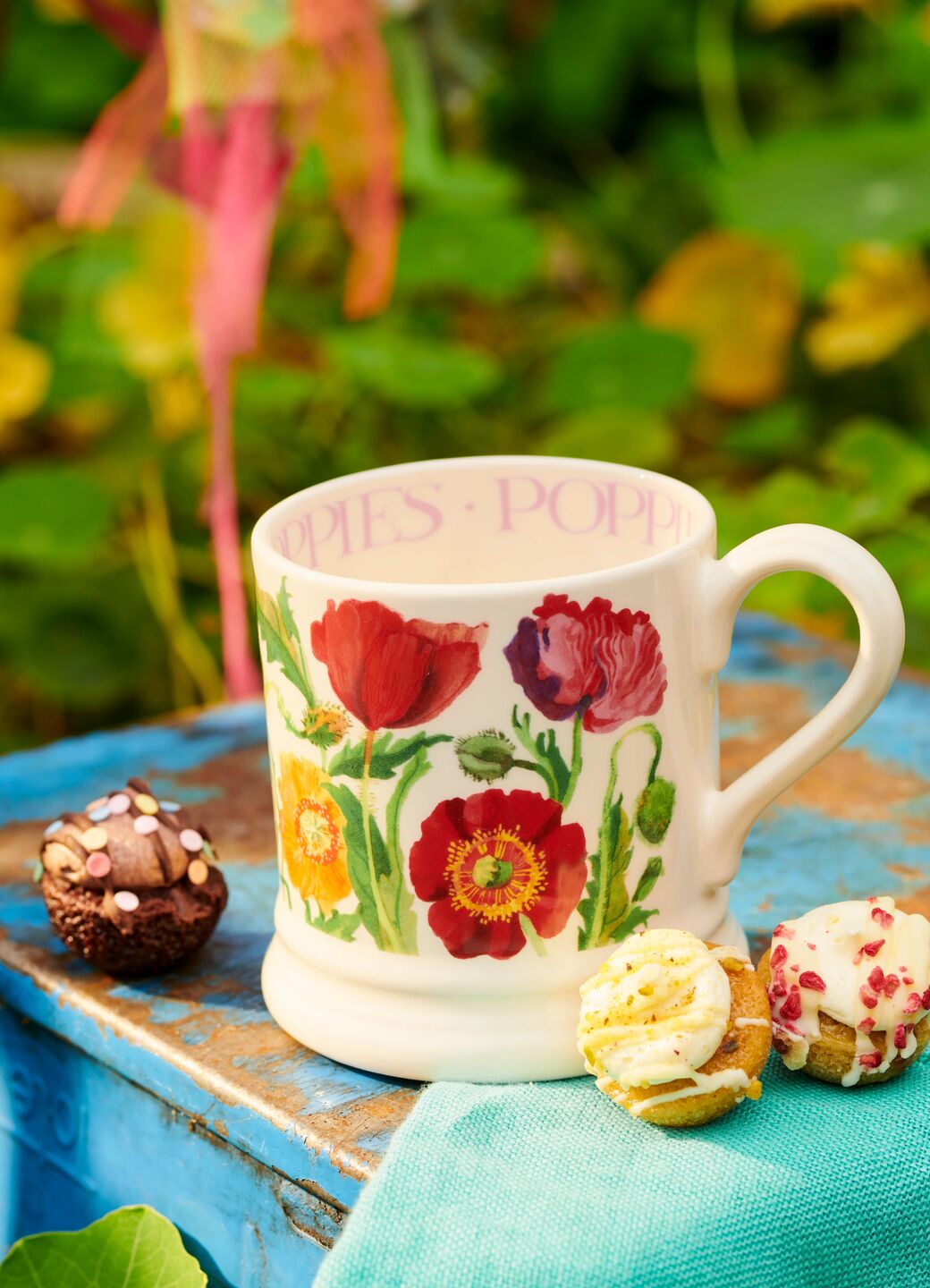 Ceramic mug with colourful poppy flower illustrations, featuring a sturdy handle, set on a rustic blue wooden table.